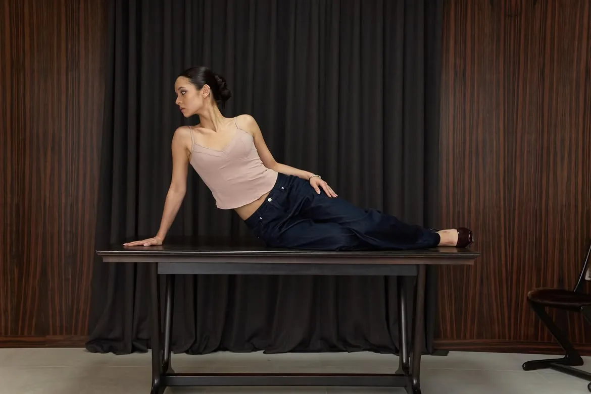 Model seated on a table leaning on one arm in a cami top